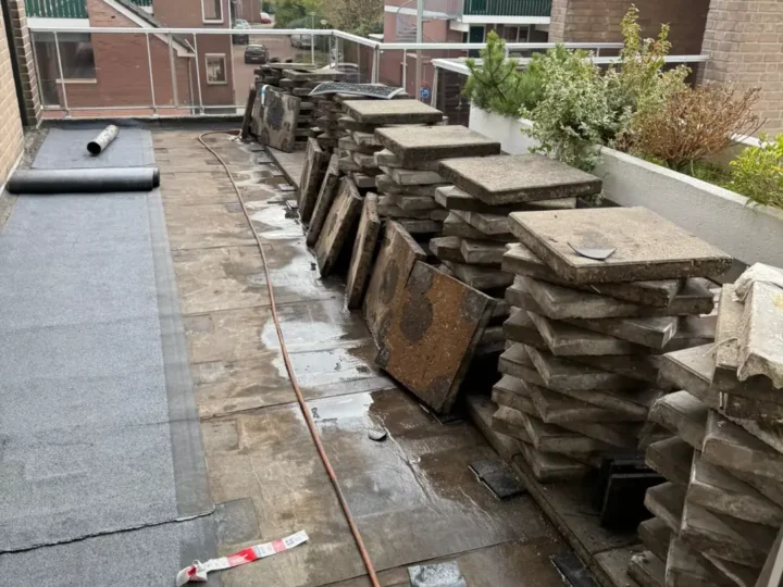 Tegels van het galerijdak opgestapeld, de nieuwe rol bitumen ligt klaar