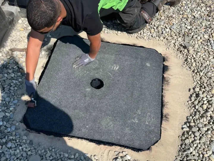 Dakdekker plakt een nieuwe bitumen manchet rond een lekkende dakafvoer in Zwijndrecht